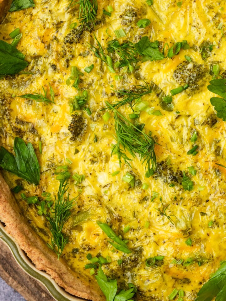 Close-up of a baked vegan quiche with a golden crust, topped with fresh herbs such as parsley and dill.