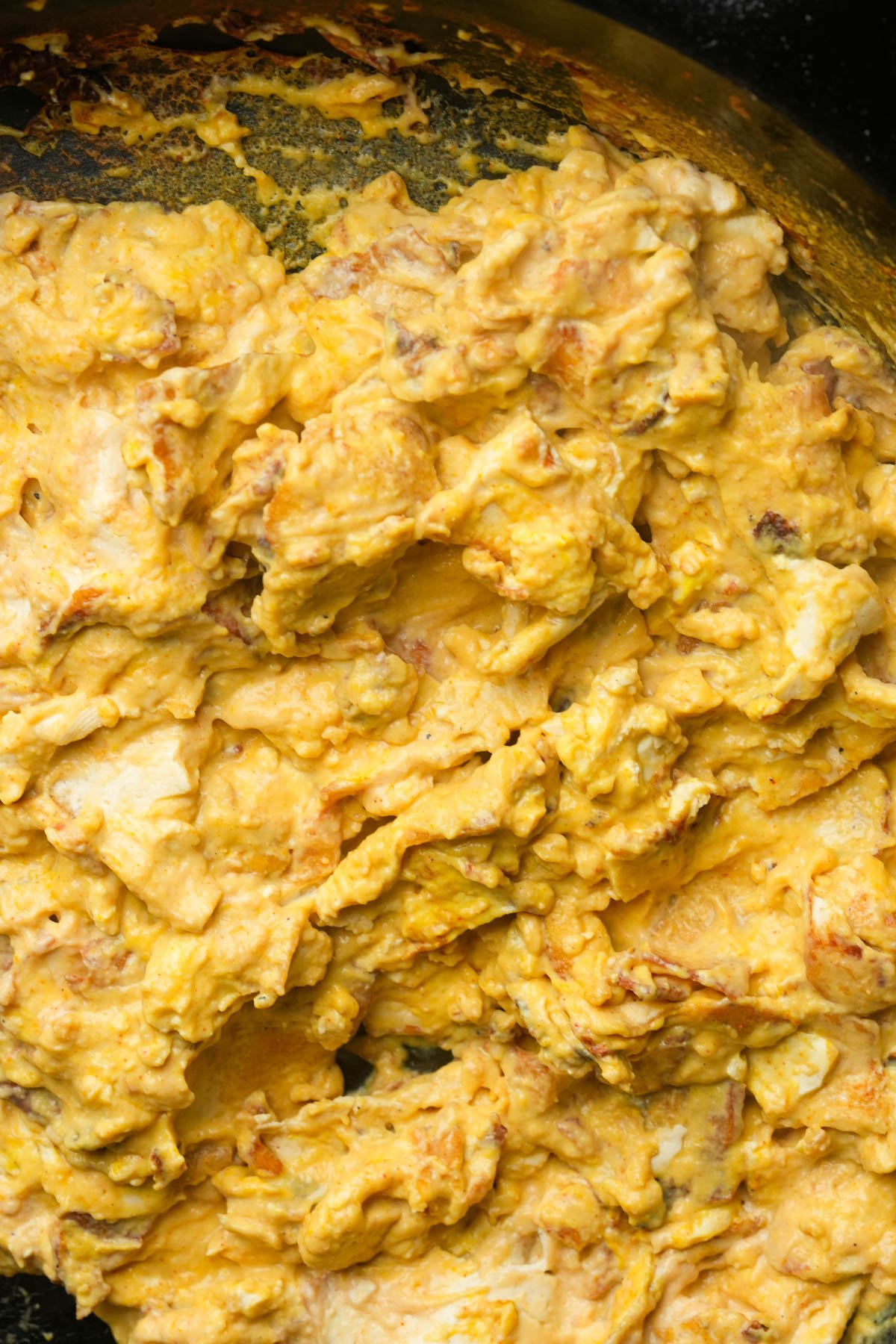 Close-up of creamy vegan scrambled eggs with a yellow hue and some browned bits, filling most of the frame.
