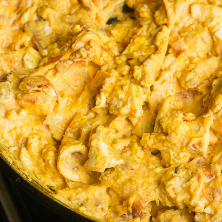 Close-up of vegan scrambled eggs cooking in a pan, showing a creamy yellow texture with some browned edges.