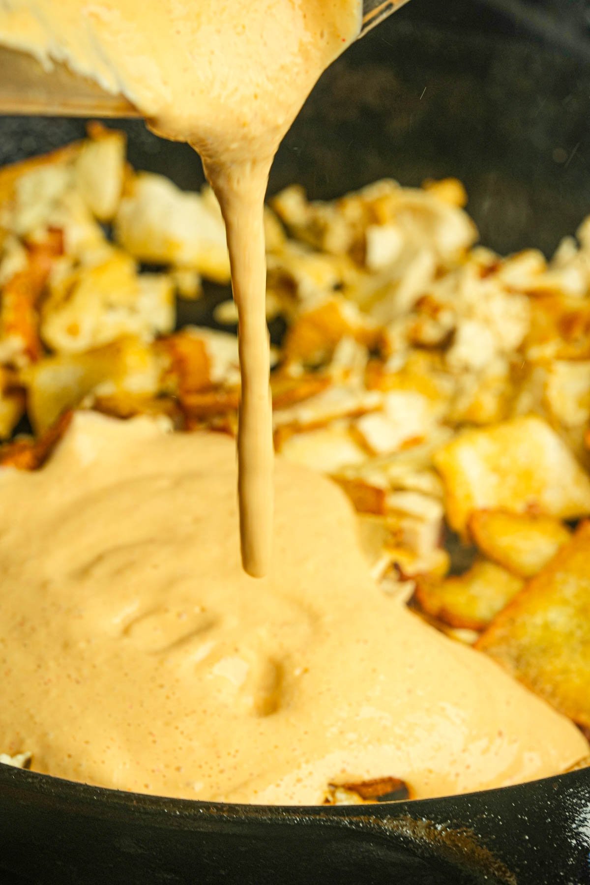 A creamy sauce is being poured over vegan scrambled eggs in a skillet.