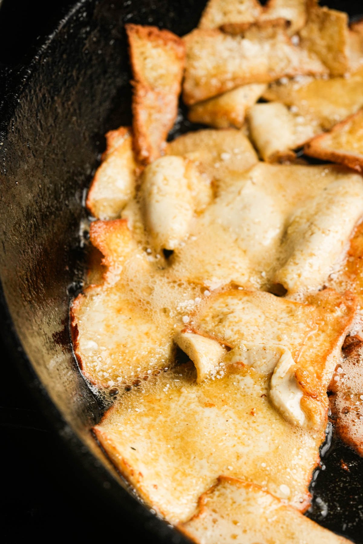 Slices of tofu frying in oil in a black skillet, with golden brown edges and visible bubbling.