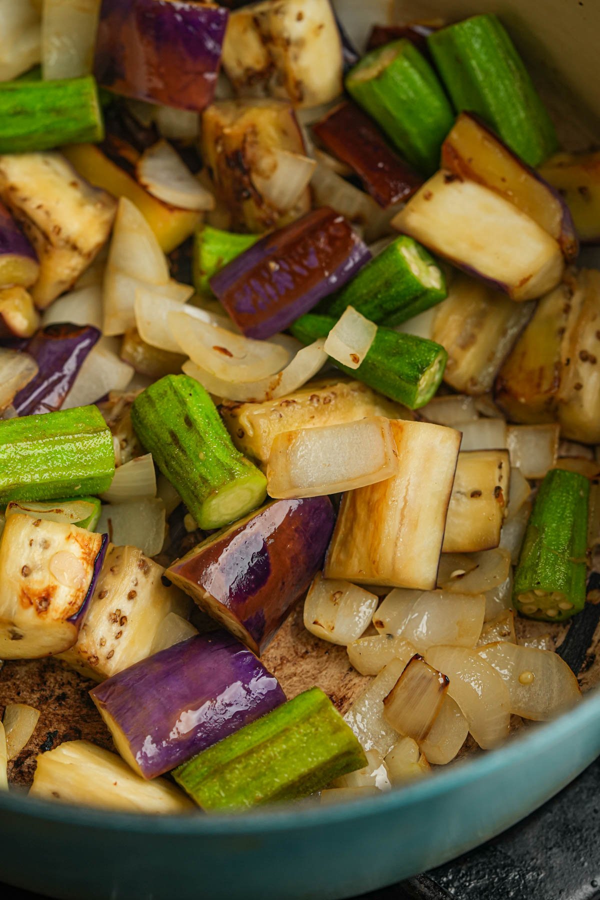 Chopped eggplant, okra, and onions are sautéing in a pan.