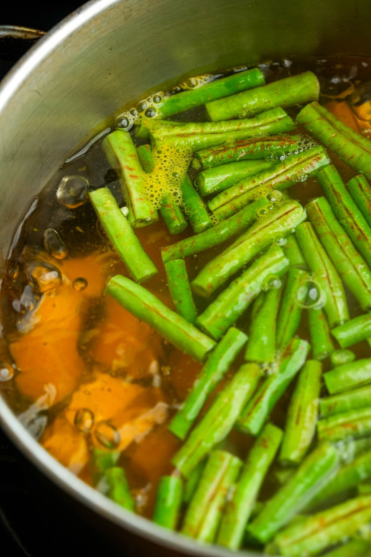 A stainless steel pot filled with simmering broth and cut green beans.