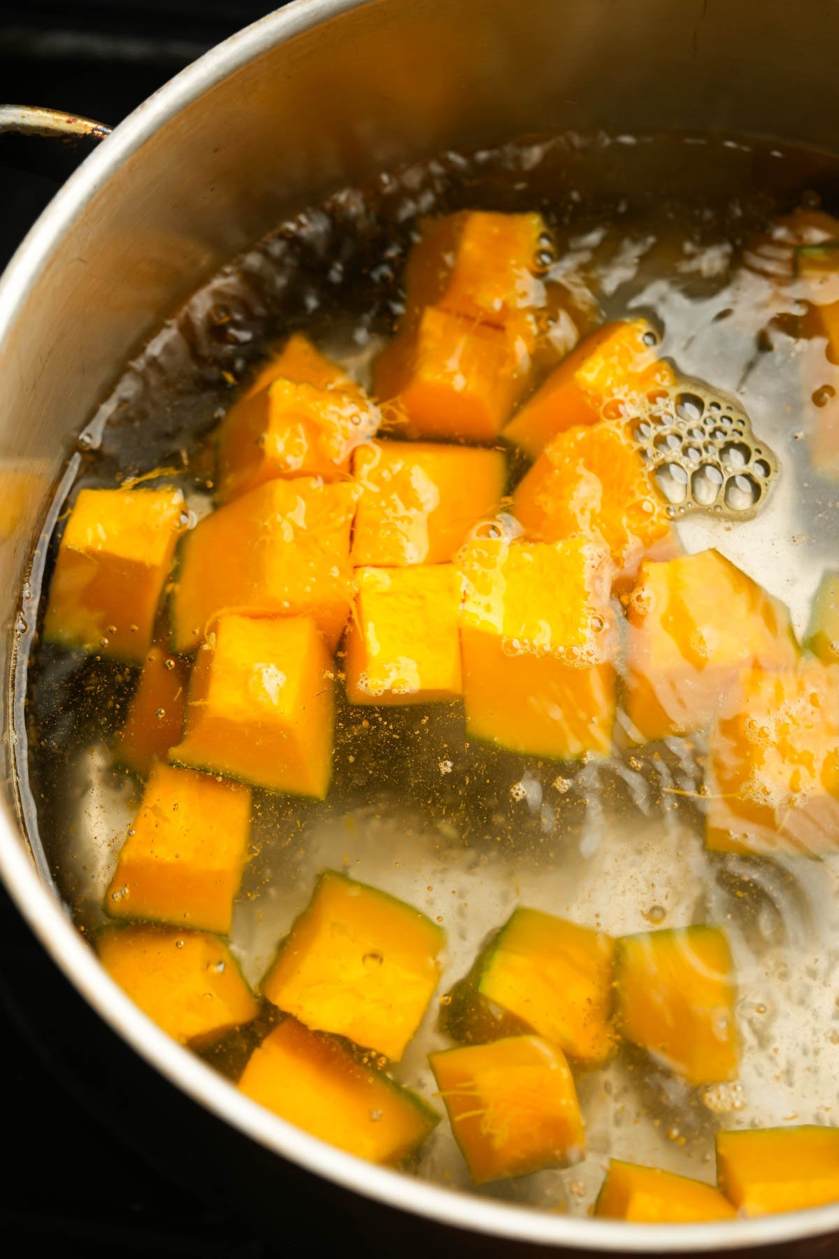 Cubed pieces of orange squash boiling in a pot of water.