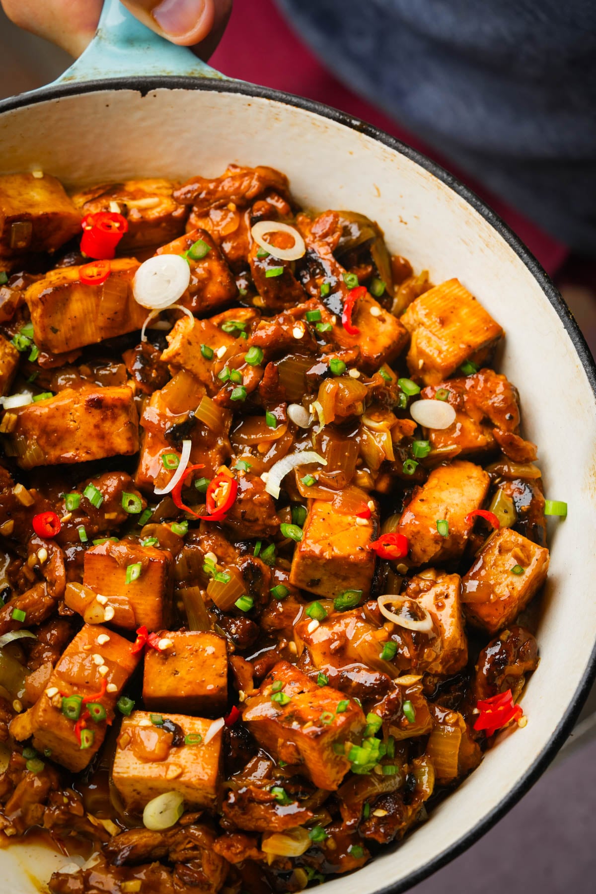 A close-up of a pan filled with stir-fried vegan tokwat baboy garnished with chopped green onions, and sliced red chili peppers in a savory sauce.