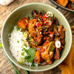 A bowl of white rice served with stir-fried tokwat baboy garnished with sliced green onions, red chili, and cilantro.
