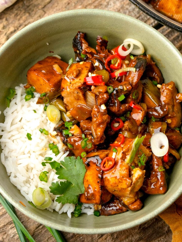 A bowl of white rice served with stir-fried tokwat baboy garnished with sliced green onions, red chili, and cilantro.