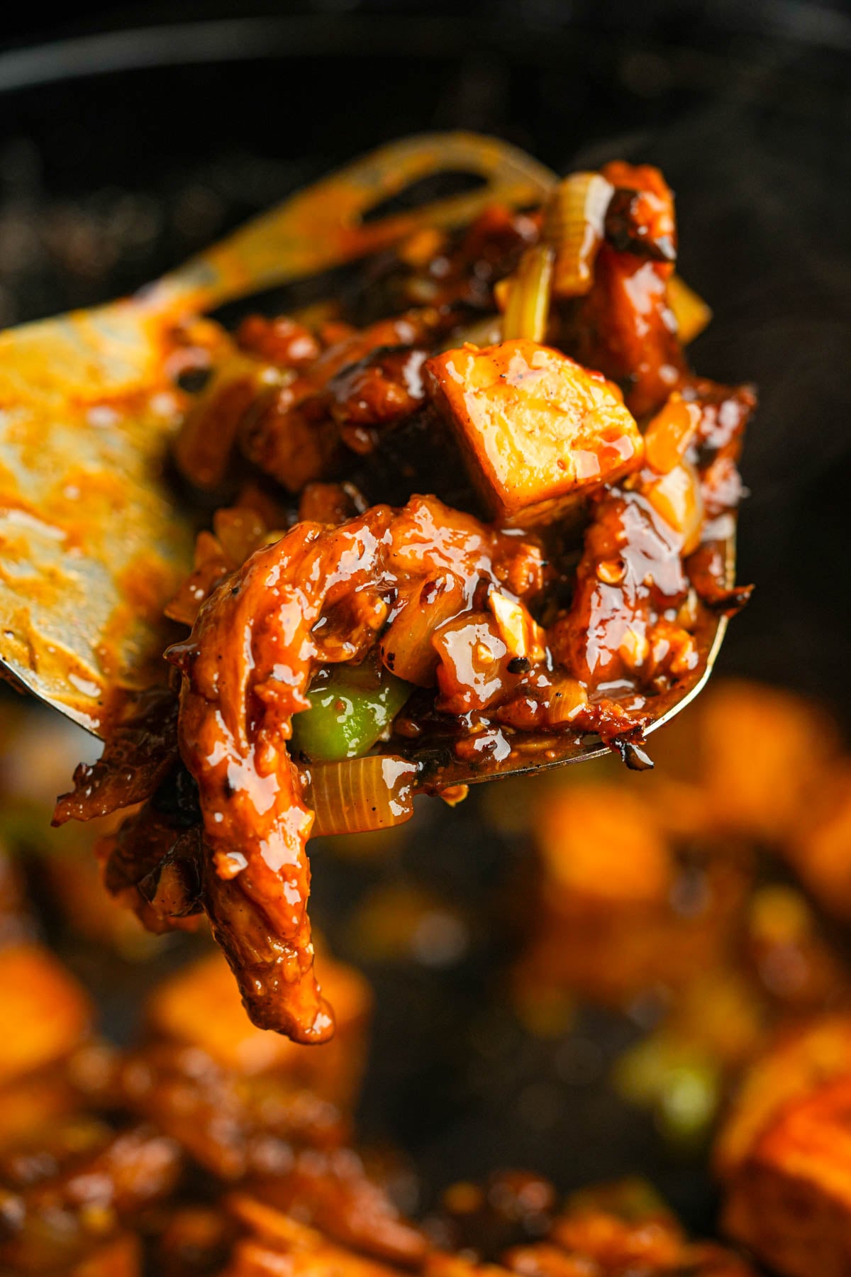 Close-up of a spatula lifting pieces of cooked tokwat baboy coated in a thick, glossy sauce.