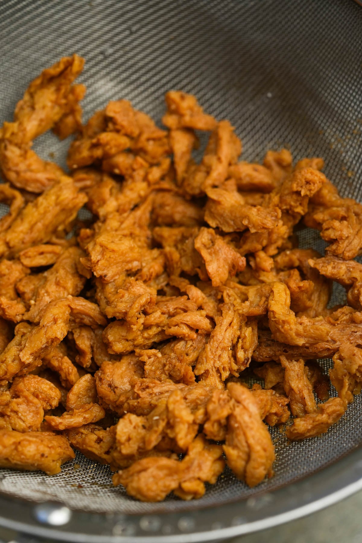 Strips of rehydrated soy curls are draining in a metal mesh strainer.