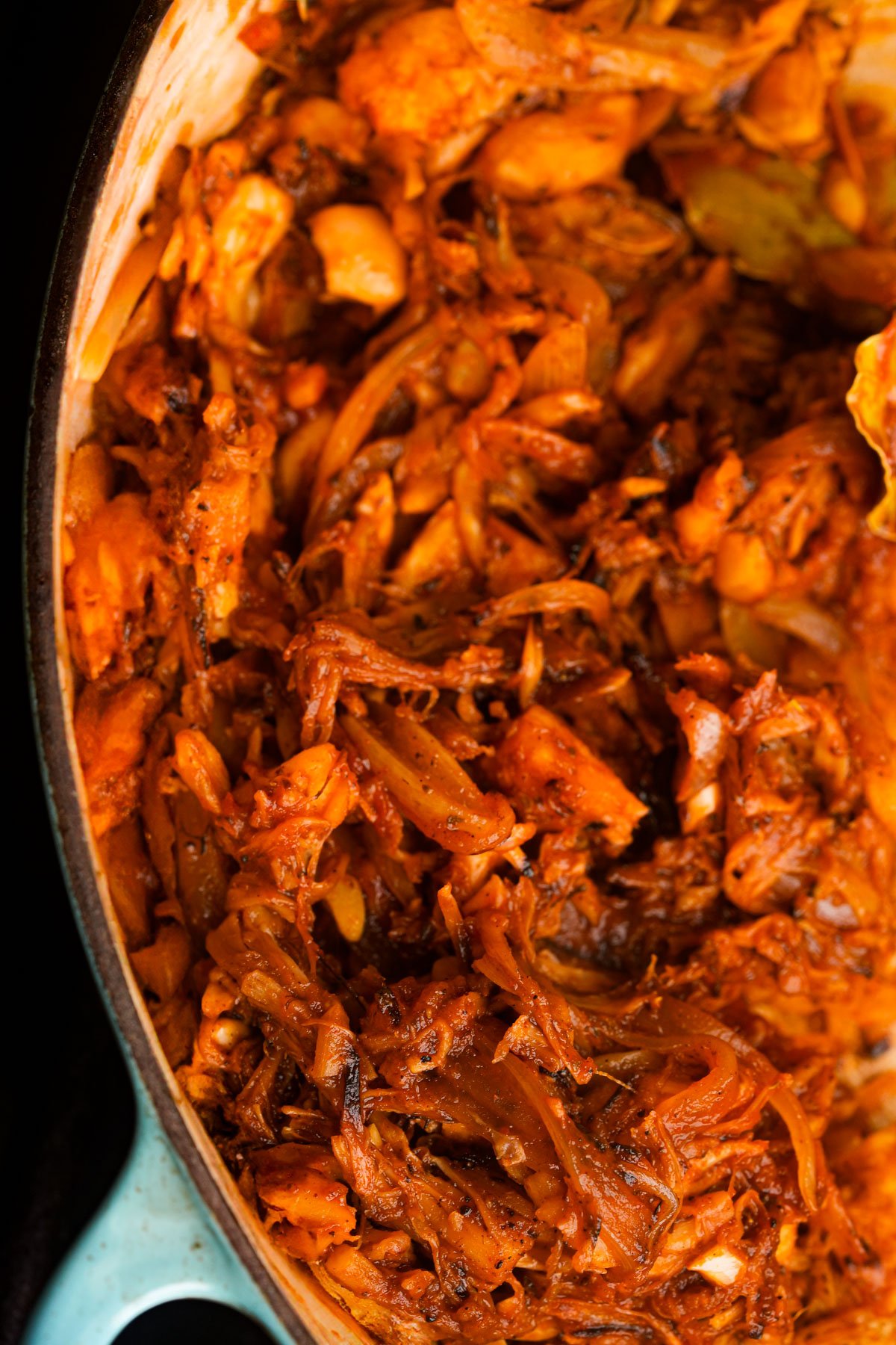 Shredded jackfruit carnitas and onions cooked in spices in a large pot or pan.