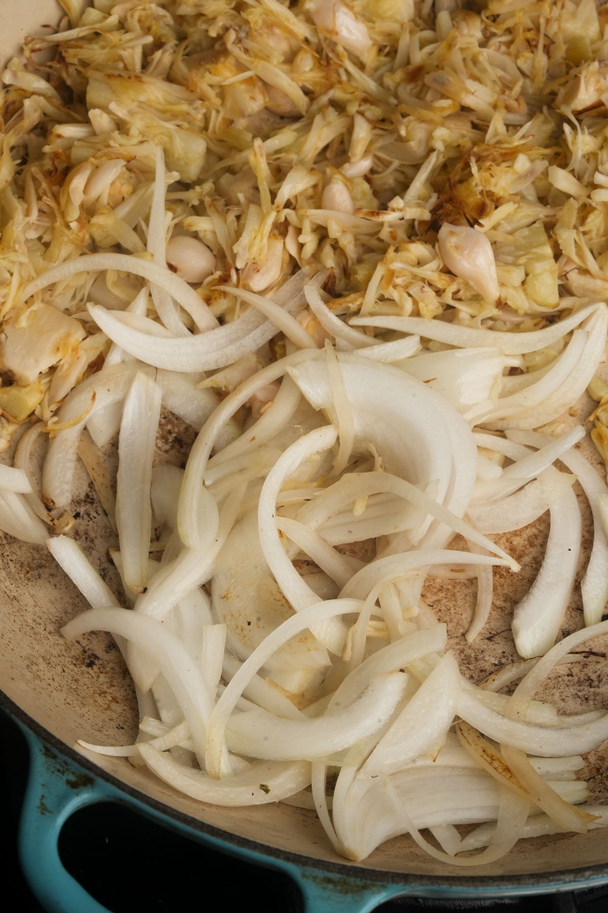 Sliced onions and jackfruit cooking in a skillet, with some pieces showing signs of browning.