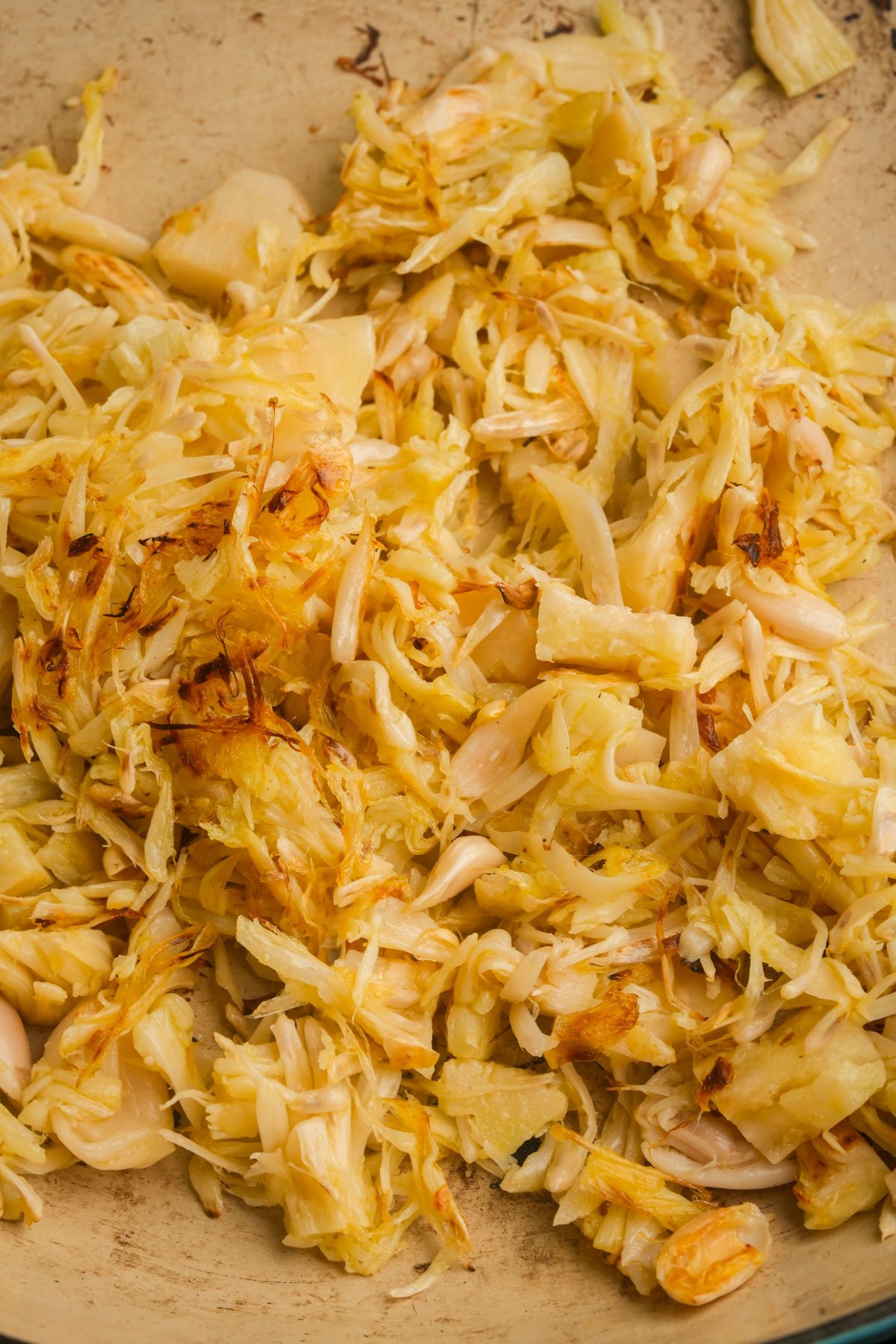 Shredded and lightly browned jackfruit pieces in a pan, showing a mix of fibrous strands and chunkier portions.