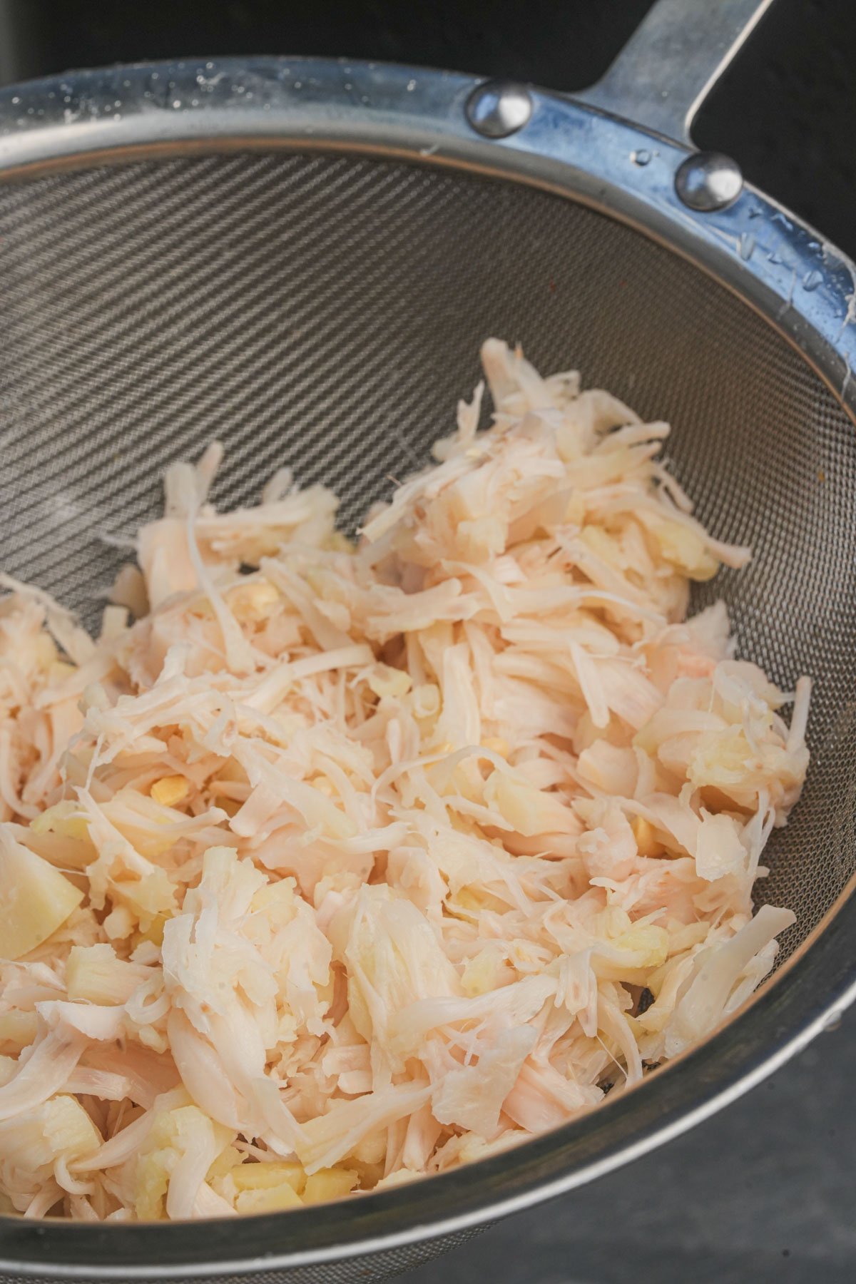 Shredded jackfruit pieces are shown in a metal strainer.