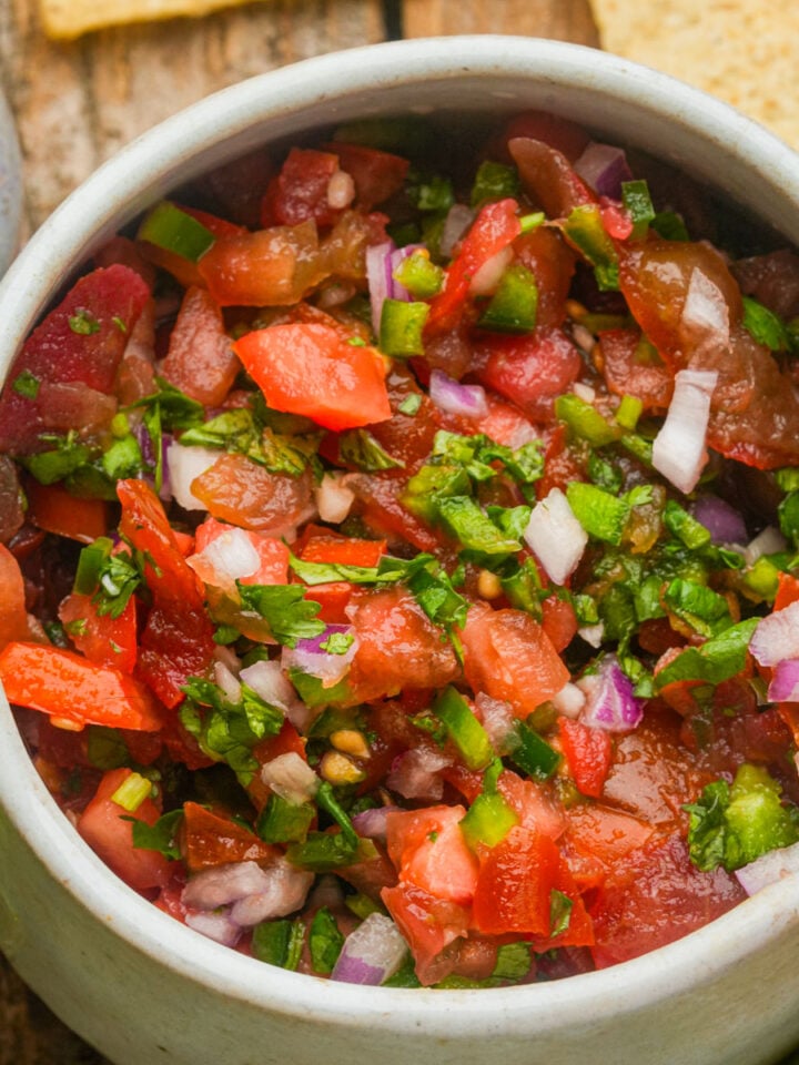 A bowl of fresh pico de gallo salsa with chopped tomatoes, onions, cilantro, and peppers on a wooden surface.