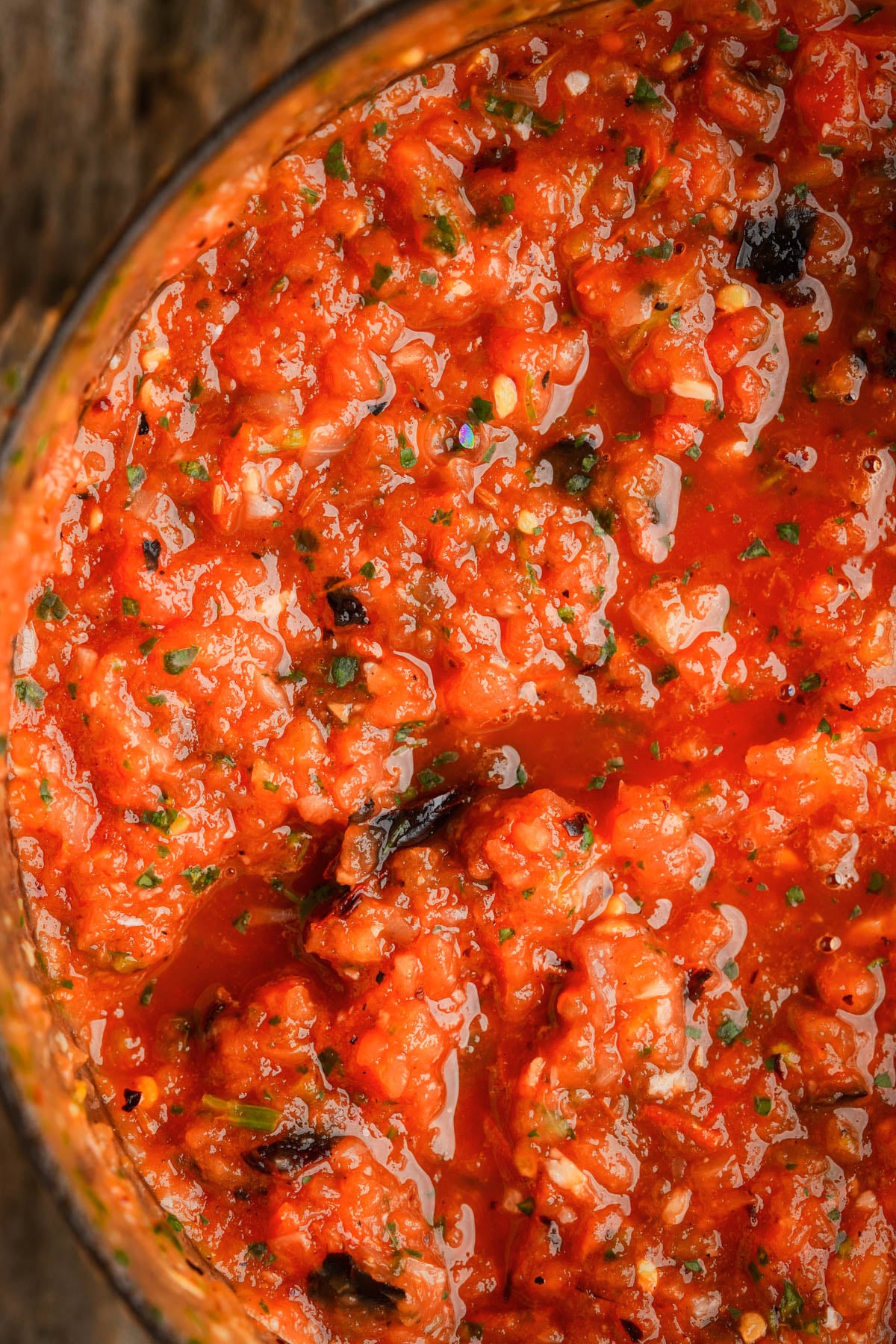 Freshly blended salsa ranchera in a food processor with visible herbs and small pieces of charred vegetables.