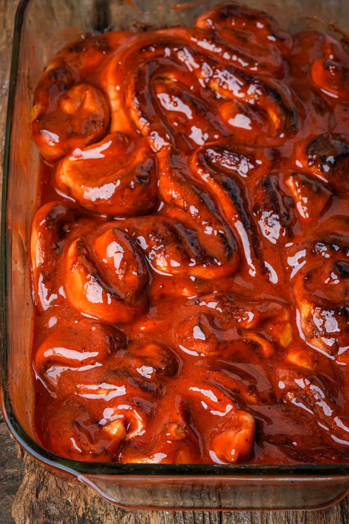 A glass baking dish filled with vegan Halloween cinnamon roll guts covered in a glossy red berry "blood", sitting on a wooden surface.