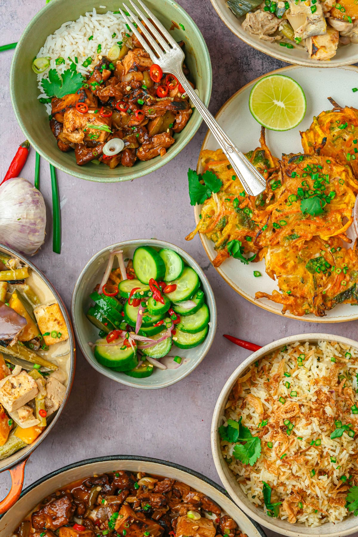 A table with bowls of Filipino food including sinangag, tokwat baboy, vegetable okoy, ginataang gulay, and ensaladang pipino.