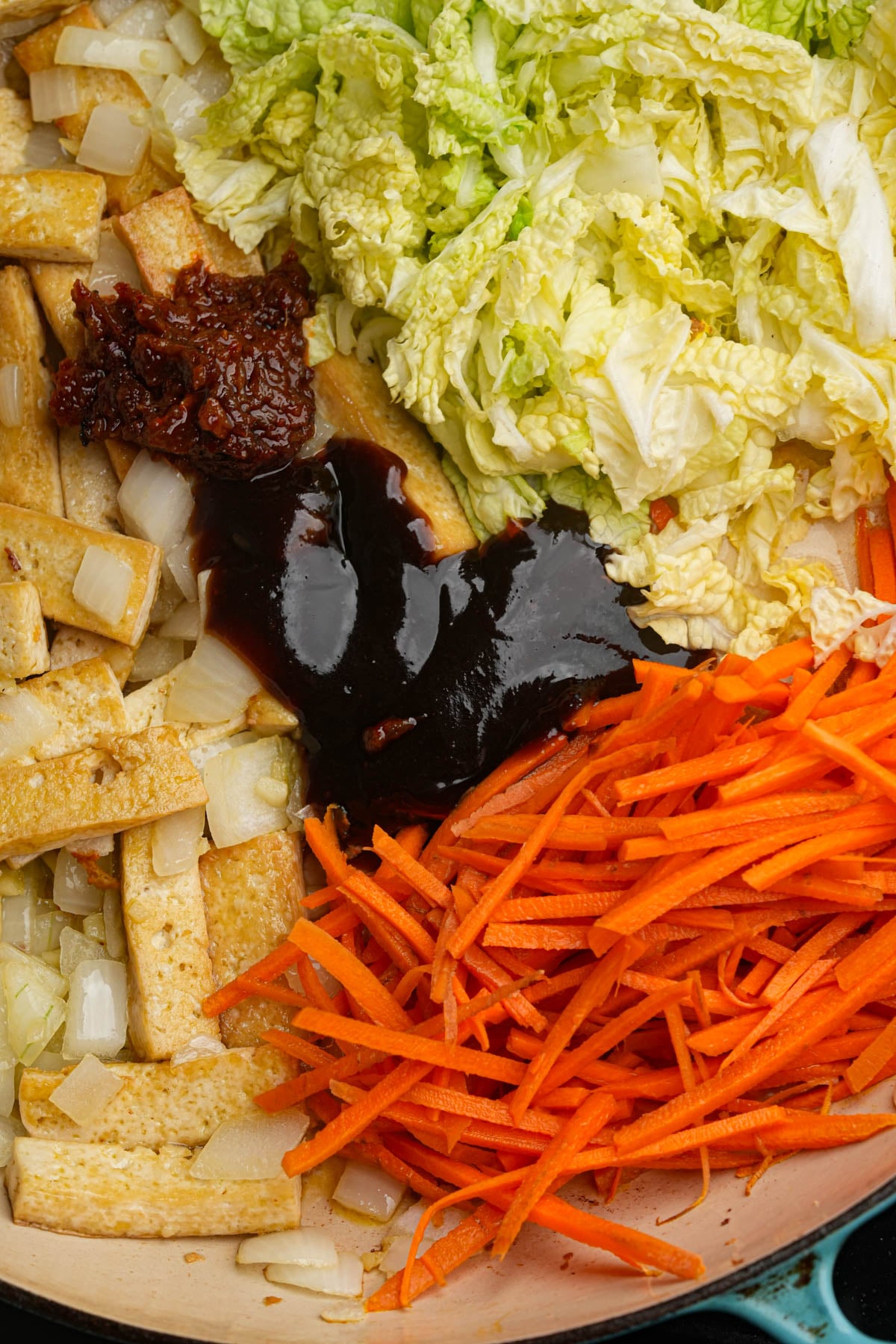 Sliced tofu, shredded carrots, chopped onions, napa cabbage, vegan shrimp paste, and vegetarian oyster sauce are cooking in a pan.