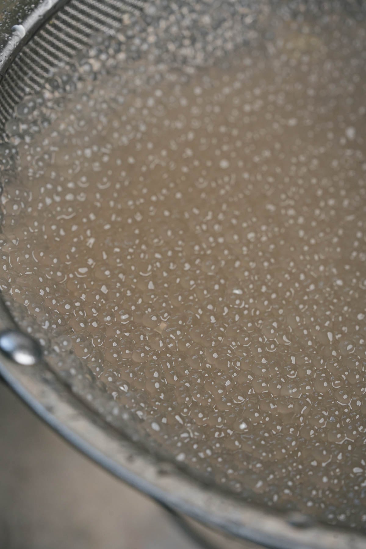 Close-up of a metal strainer holding drained tapioca pearls.