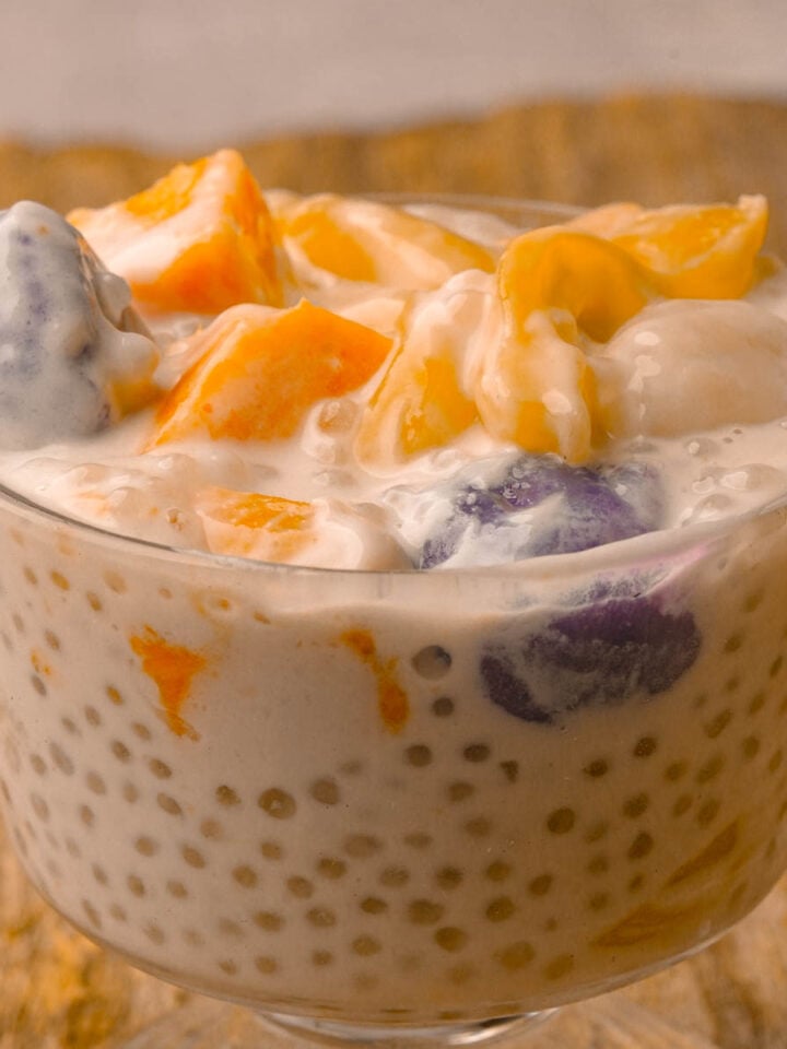 A glass bowl filled with ginataang bilo bilo with tapioca pearls, sweet potato chunks, and purple ube dumplings, jackfruit pieces, set on a wooden surface.