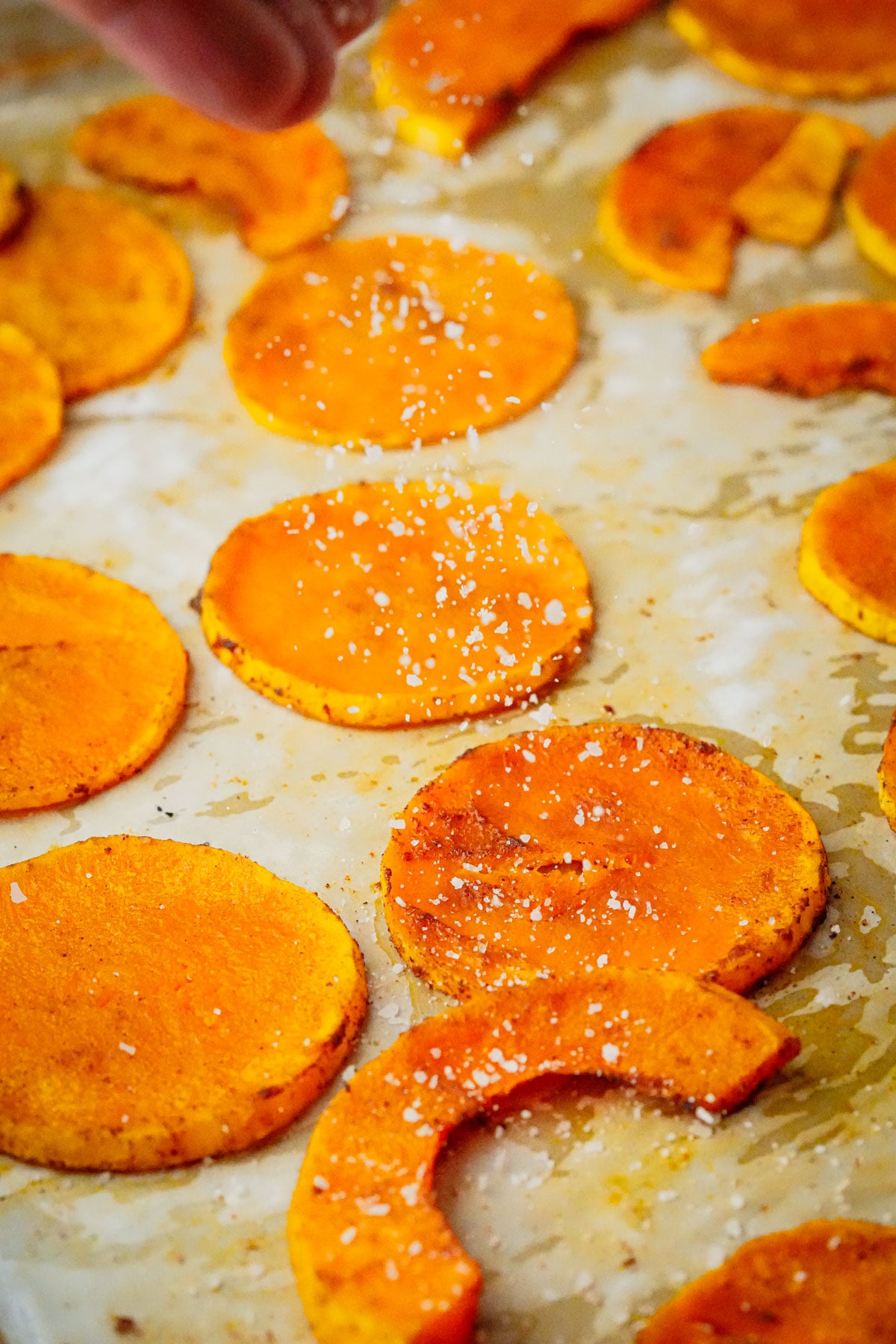 Baked squash slices sprinkled with coarse salt, with a hand visible at the top adding more salt.