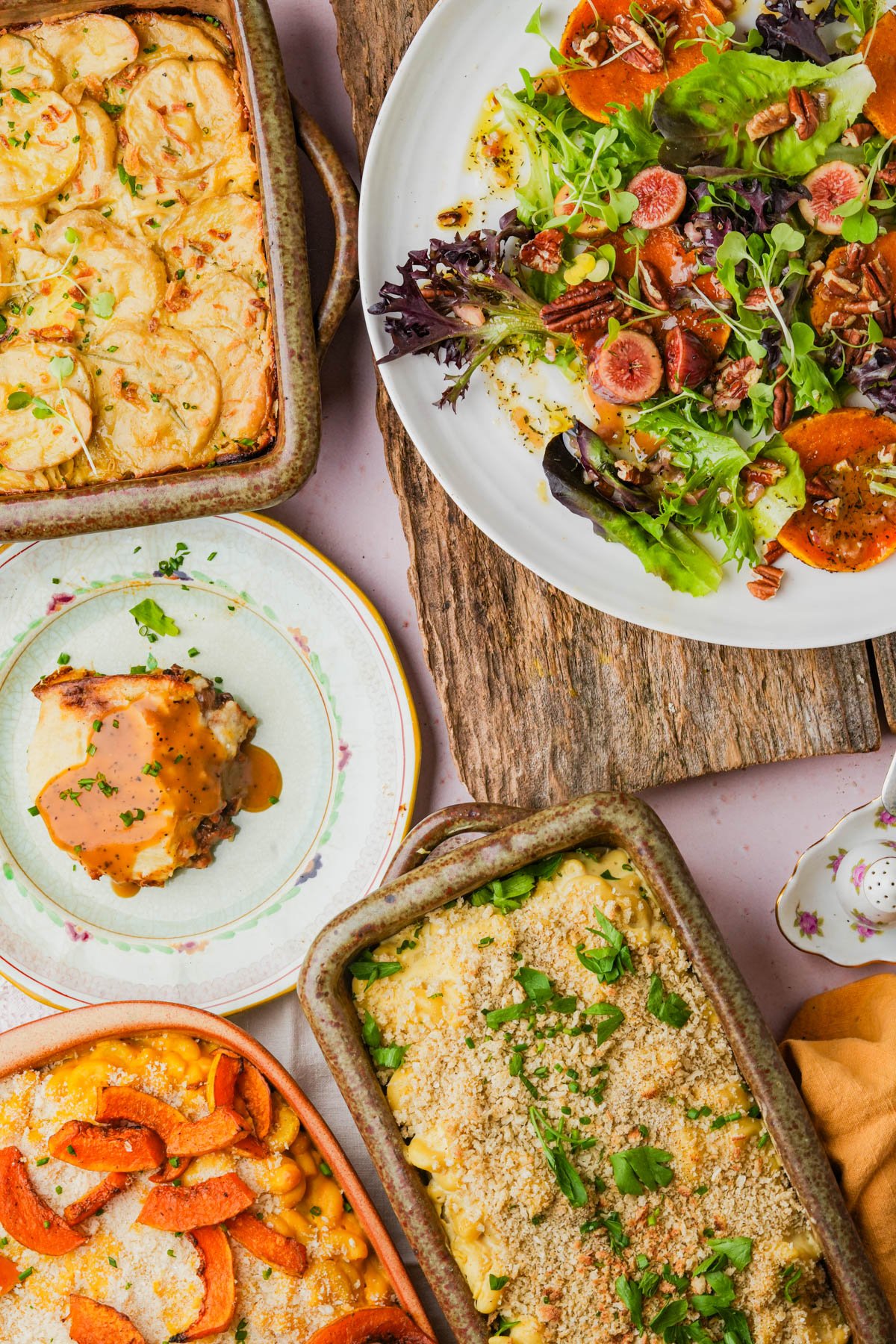 A table set with vegan butternut squash macaroni and cheese, vegan truffle macaroni and cheese, a butternut squash salad topped with figs and pecans, a slice of vegan shepherd's pie, all presented in rustic ceramic dishes.