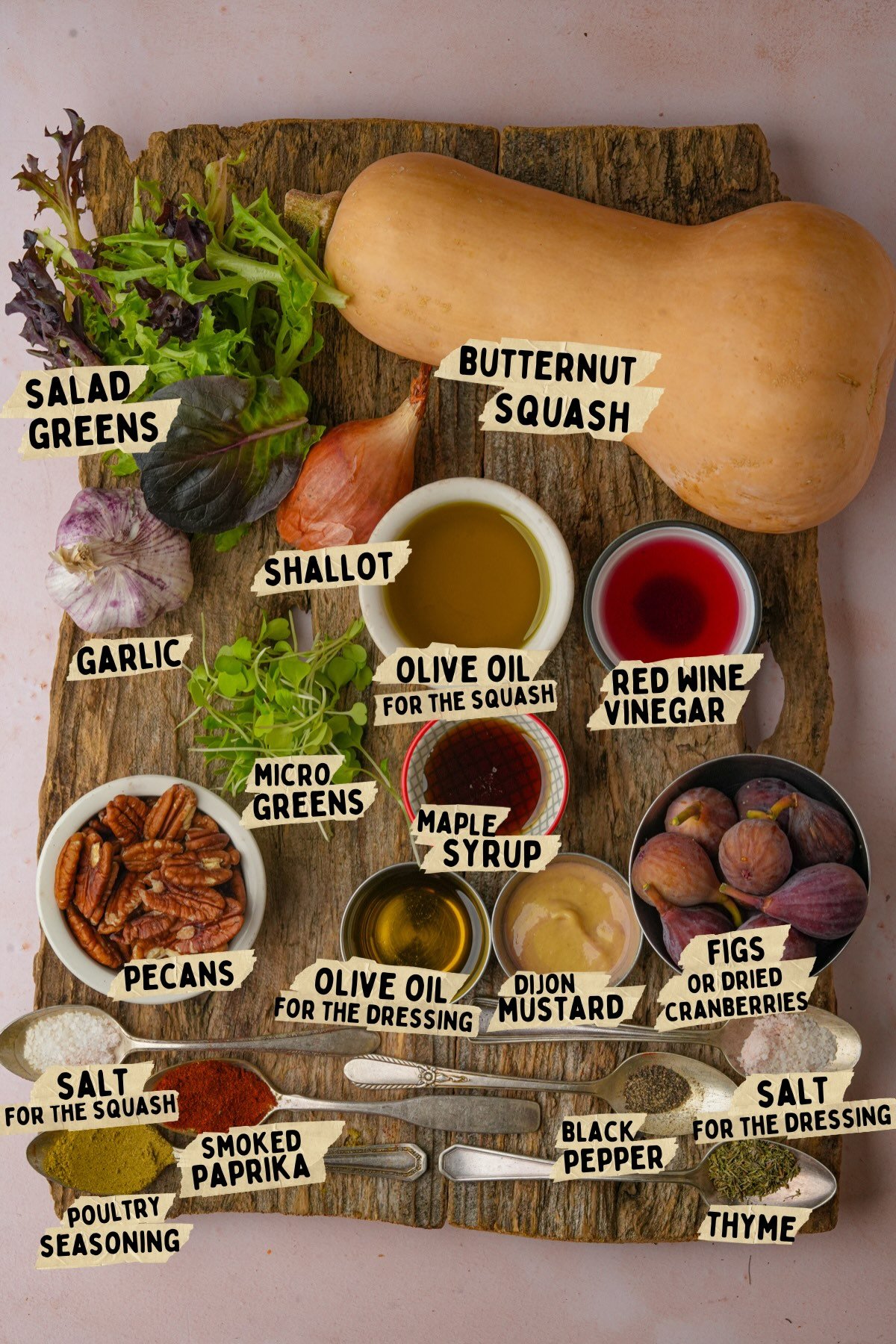 A wooden board displaying labeled ingredients for a butternut squash salad recipe: salad greens, butternut squash, garlic, shallot, olive oil, plum vinegar, micro greens, maple syrup, pecans, Dijon mustard, figs, salt, smoked paprika, black pepper, thyme, and poultry seasoning.