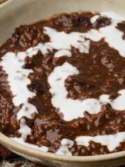 A close-up of a bowl filled with creamy vegan champorado topped with a swirl of white cream.