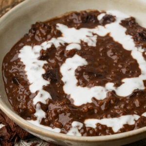 A close-up of a bowl filled with creamy vegan champorado topped with a swirl of white cream.