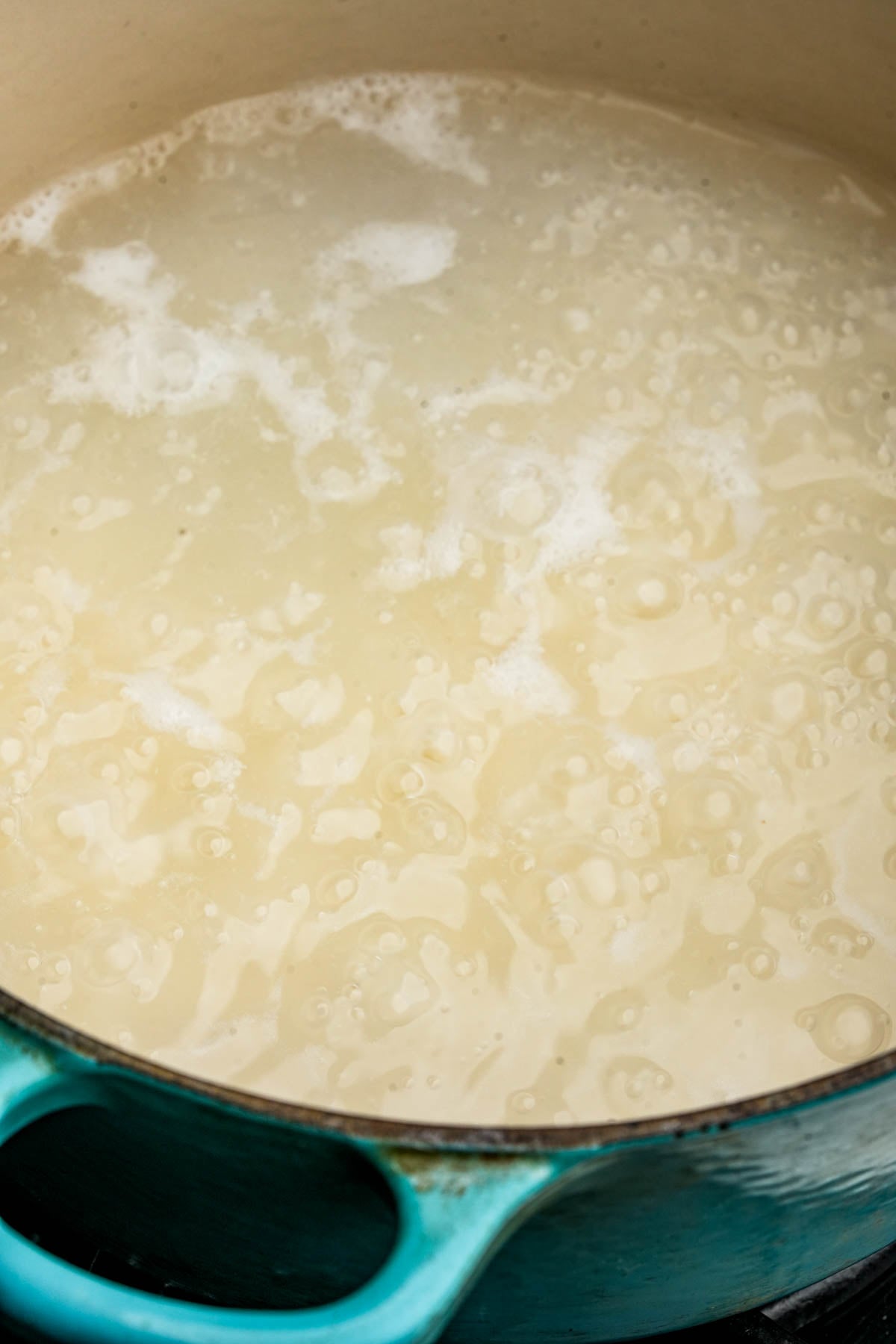 A close-up of a teal pot filled with bubbling water and sweet rice cooking on a stovetop.