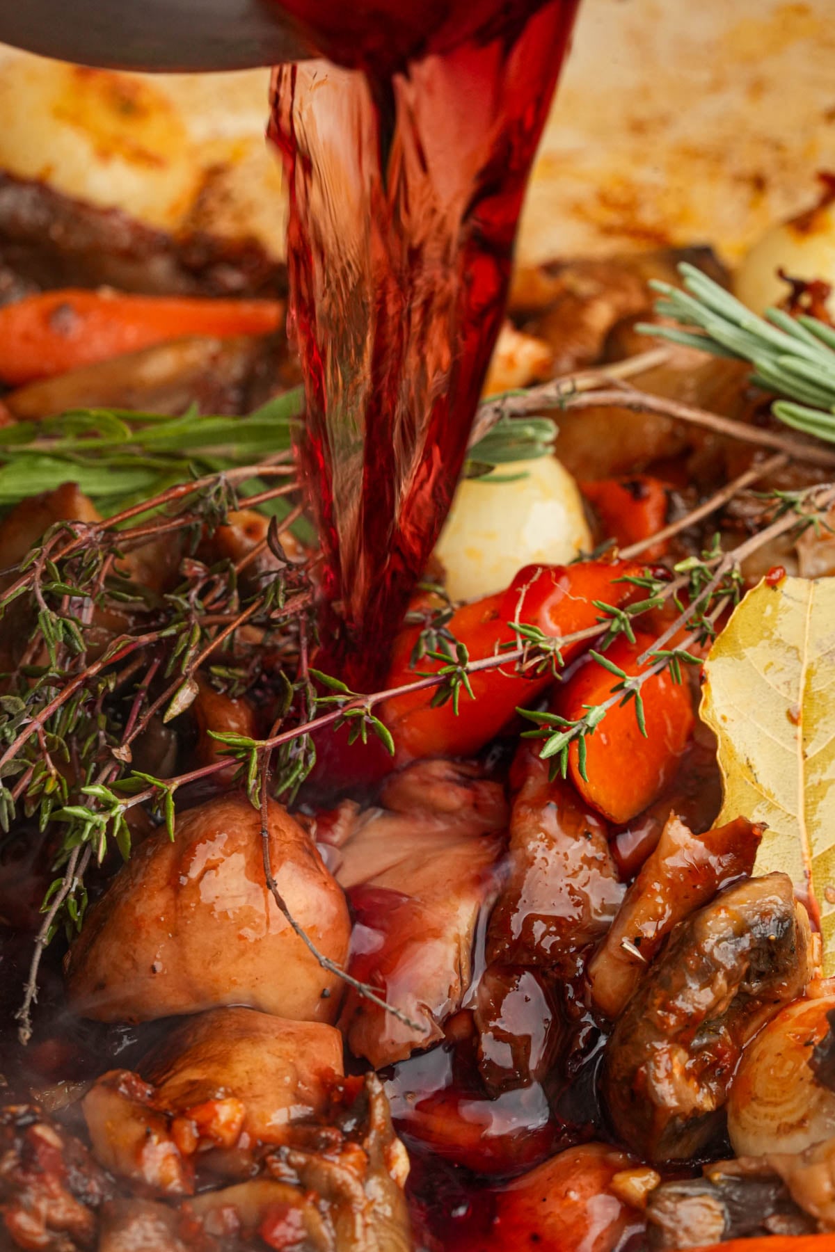 Red wine being poured over a pan of cooking mushroom bourguignon.