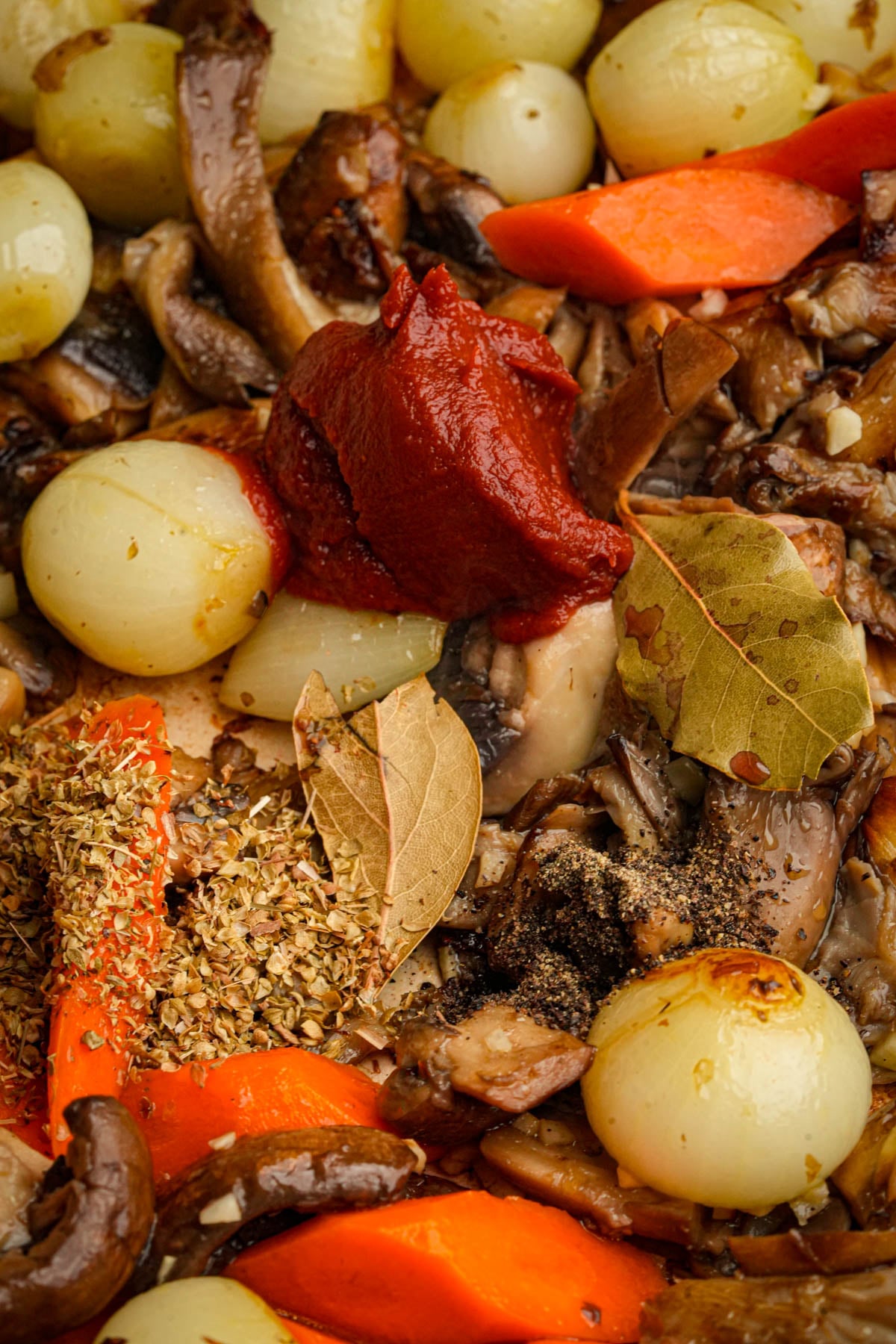 Tomato paste and herbs are added to the cooking pearl onions, carrot slices, and mushrooms to make a batch of mushroom bourguignon.