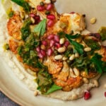 A plate of roasted cauliflower steak with bean puree, parsley sauce and pine nuts.