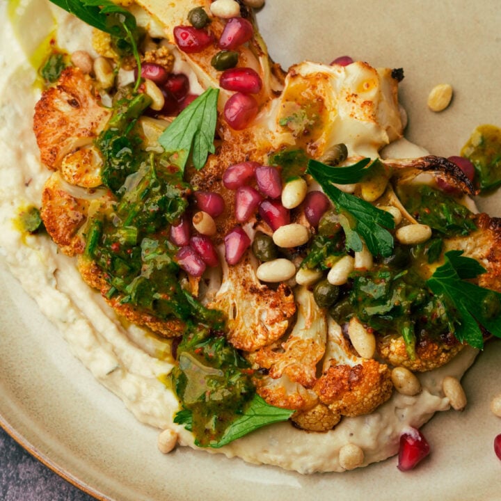 A plate of roasted cauliflower steak with bean puree, parsley sauce and pine nuts.
