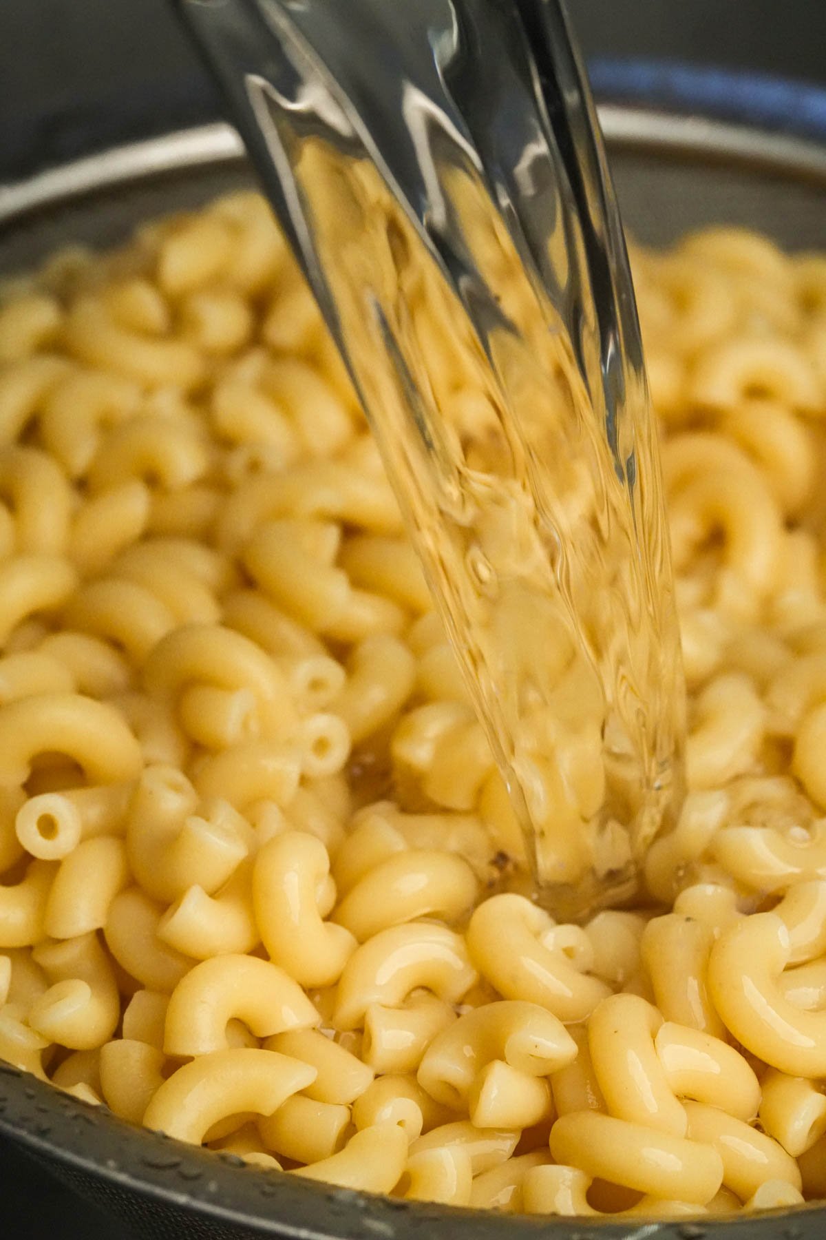 Water being poured over cooked elbow macaroni pasta in a colander.
