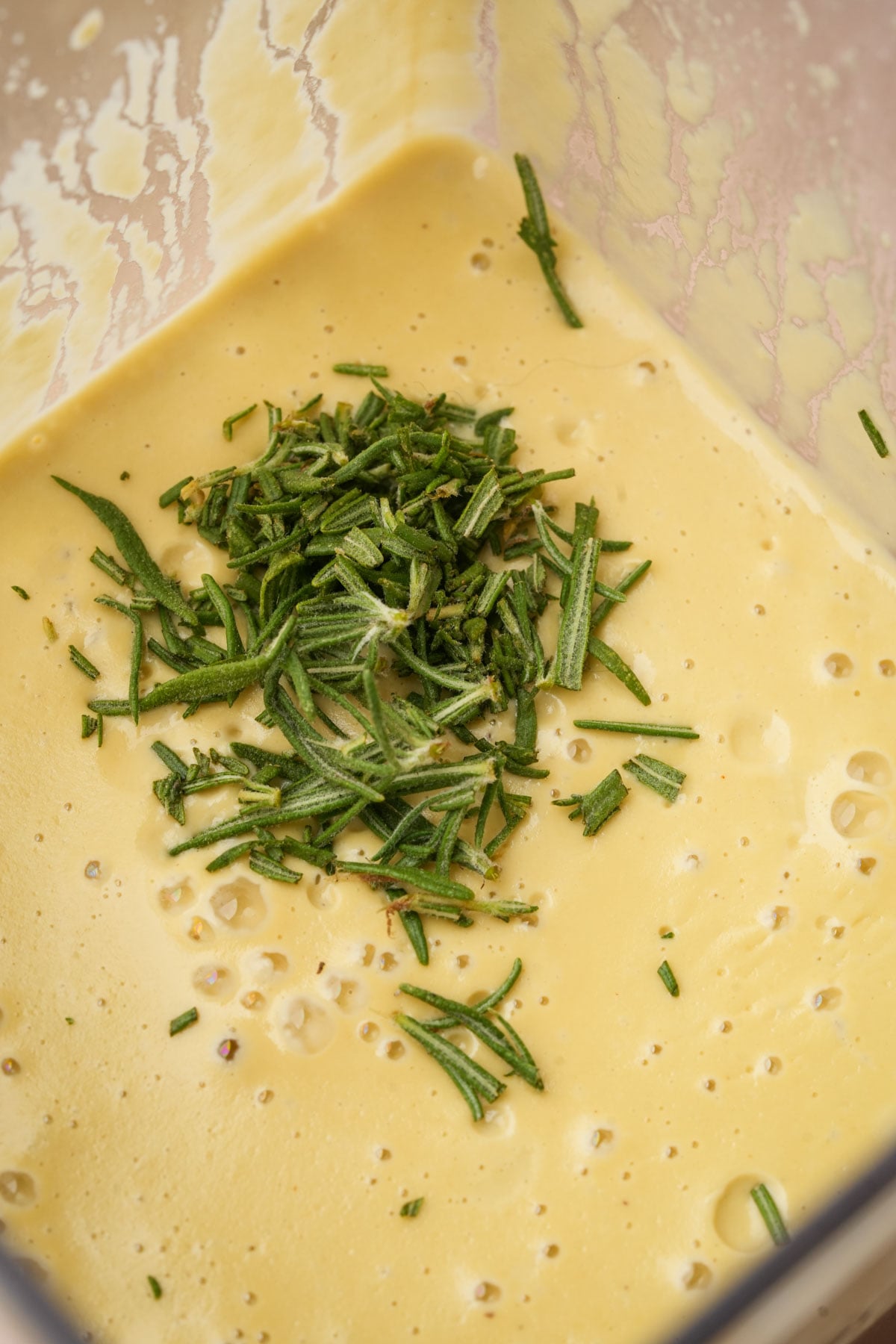 A close-up of a creamy yellow sacue in a blender with freshly chopped rosemary sprinkled on top.