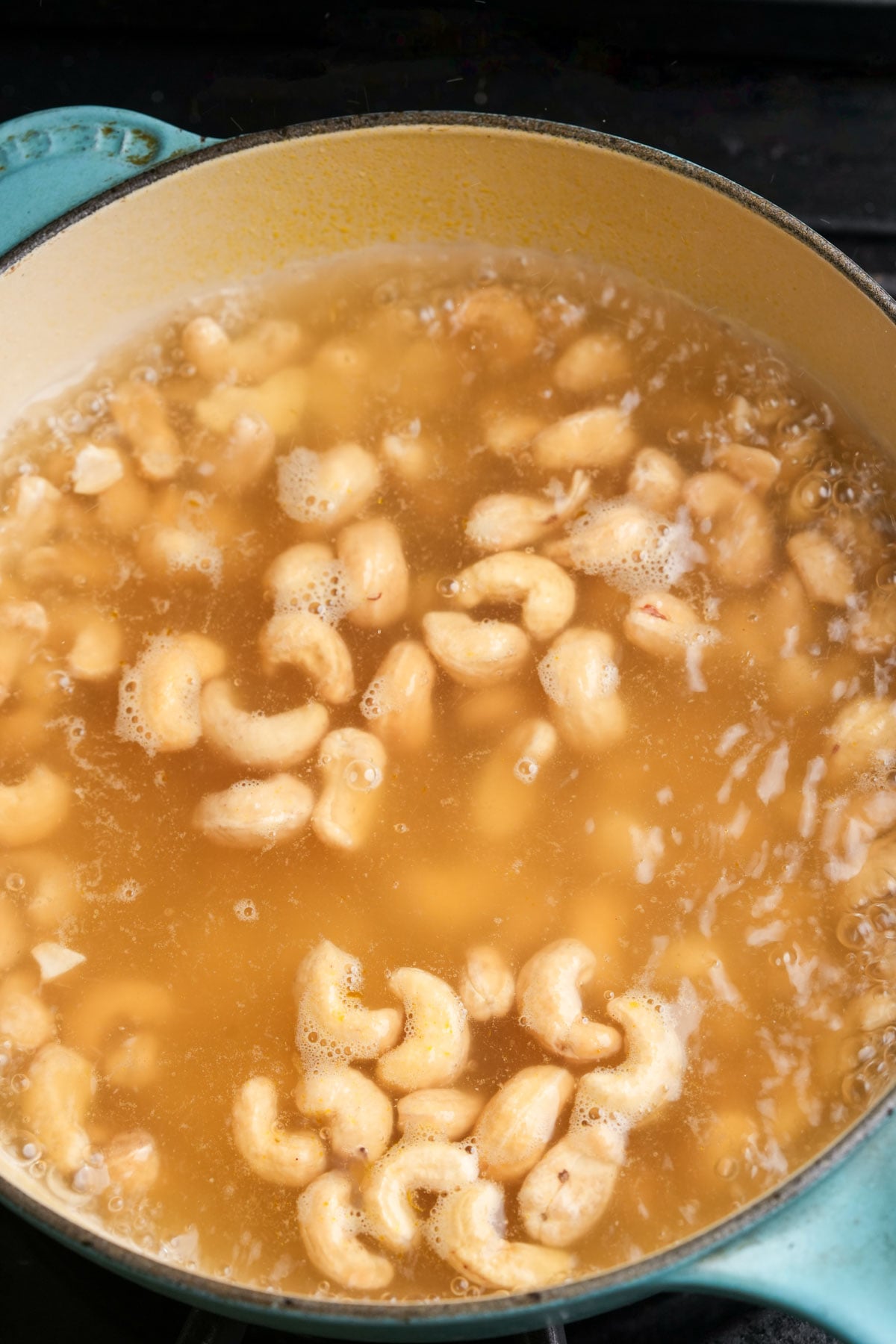 A pot filled with simmering broth and raw cashews being boiled, with bubbles and foam forming on the surface.