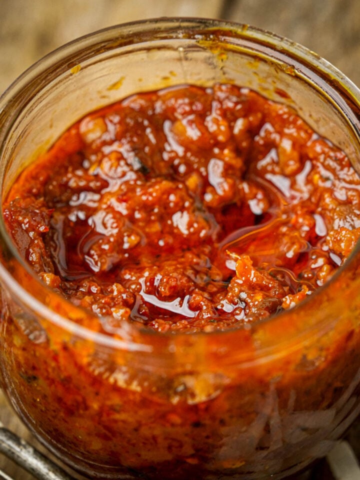 A close-up of a glass jar filled with chunky, red vegan shrimp paste placed on a rustic wooden table.