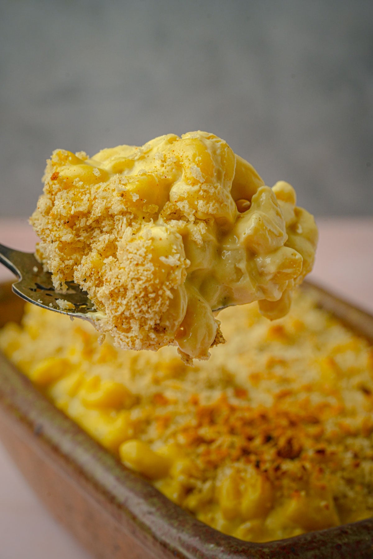 A close-up of a fork holding a creamy serving of baked vegan truffle macaroni and cheese with a golden breadcrumb topping.