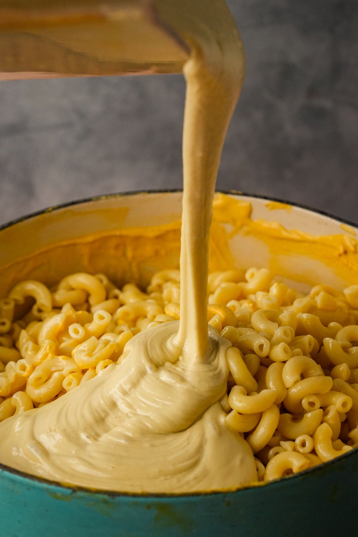 Creamy truffle cheese sauce being poured over a pot of cooked macaroni noodles, ready to be mixed for homemade vegan truffle macaroni and cheese.
