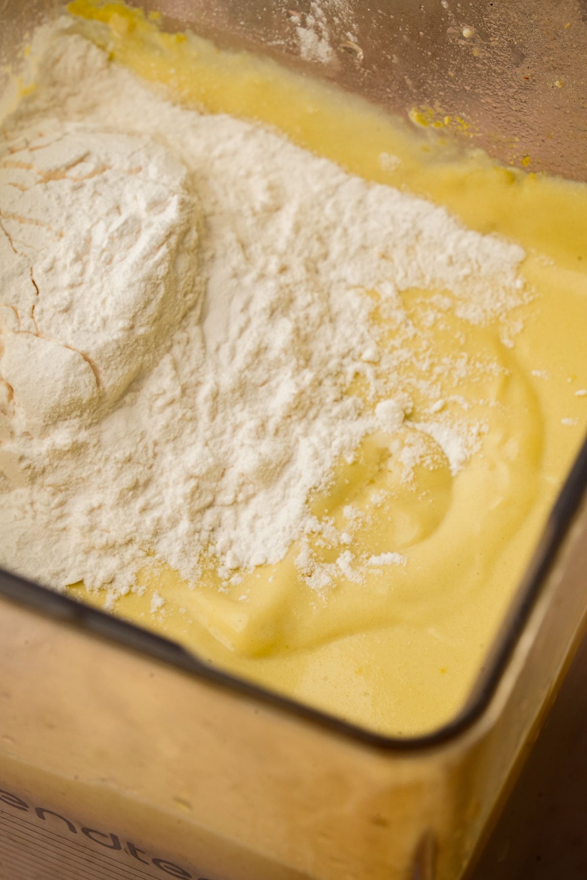 Close-up of a mixing bowl containing a yellow vegan cheese sauce with a mound of white starch sitting on top, ready to be mixed together.