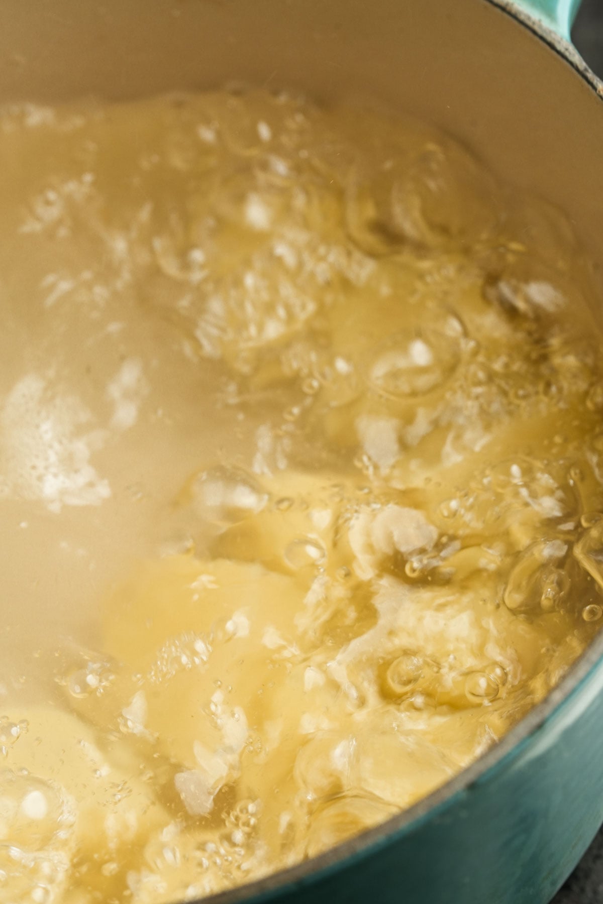 A close-up of pasta boiling in a pot of water with potatoes in it.