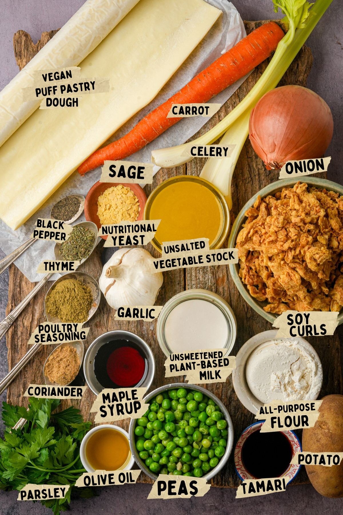 A variety of labeled ingredients for a vegan pot pie are arranged on a wooden board, including puff pastry dough, carrot, celery, onion, soy curls, peas, potato, plant-based milk, olive oil, spices, and seasonings.