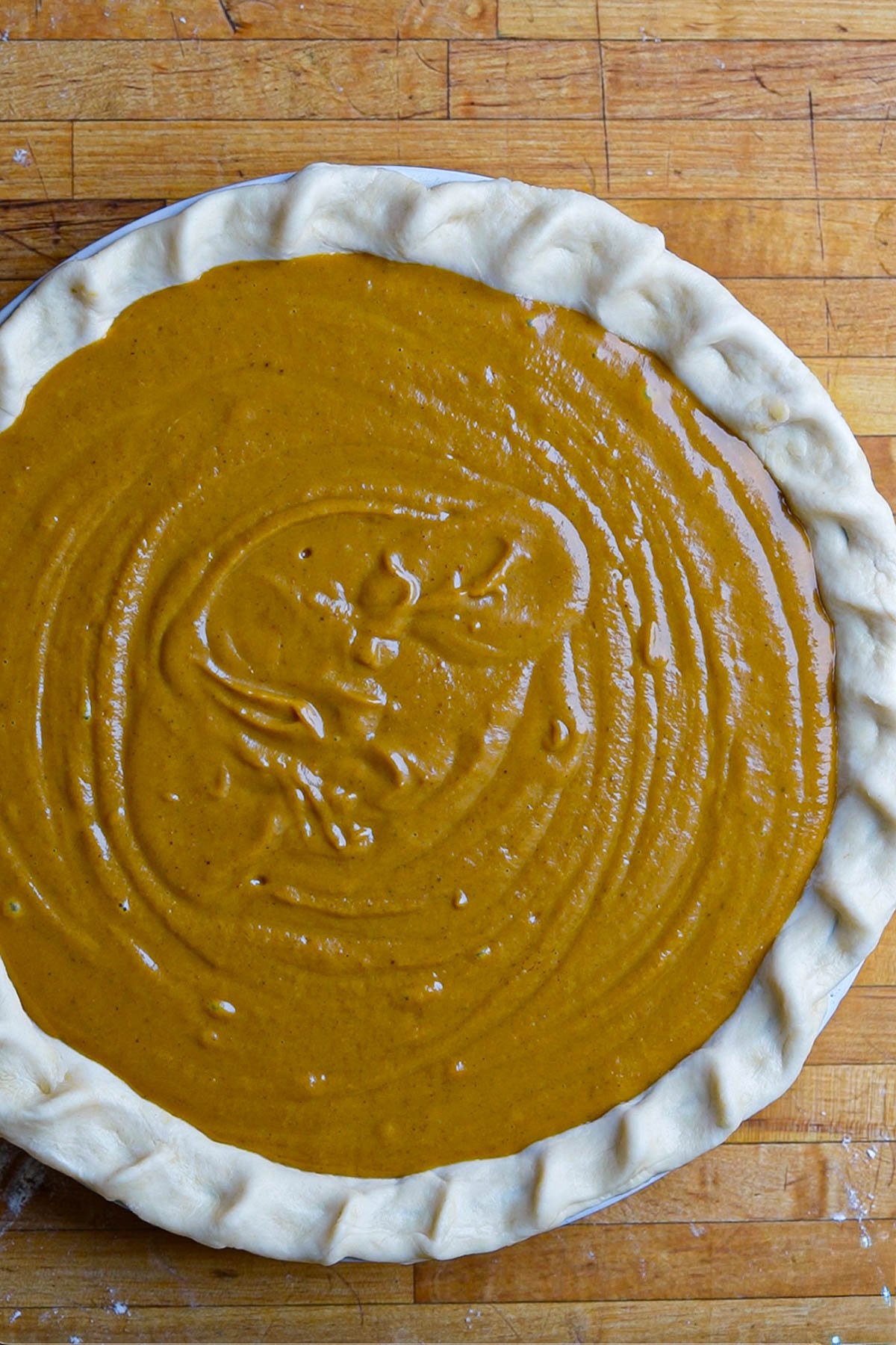 Unbaked vegan pumpkin pie with a crimped crust and smooth, orange filling sits on a wooden surface, ready to be baked.