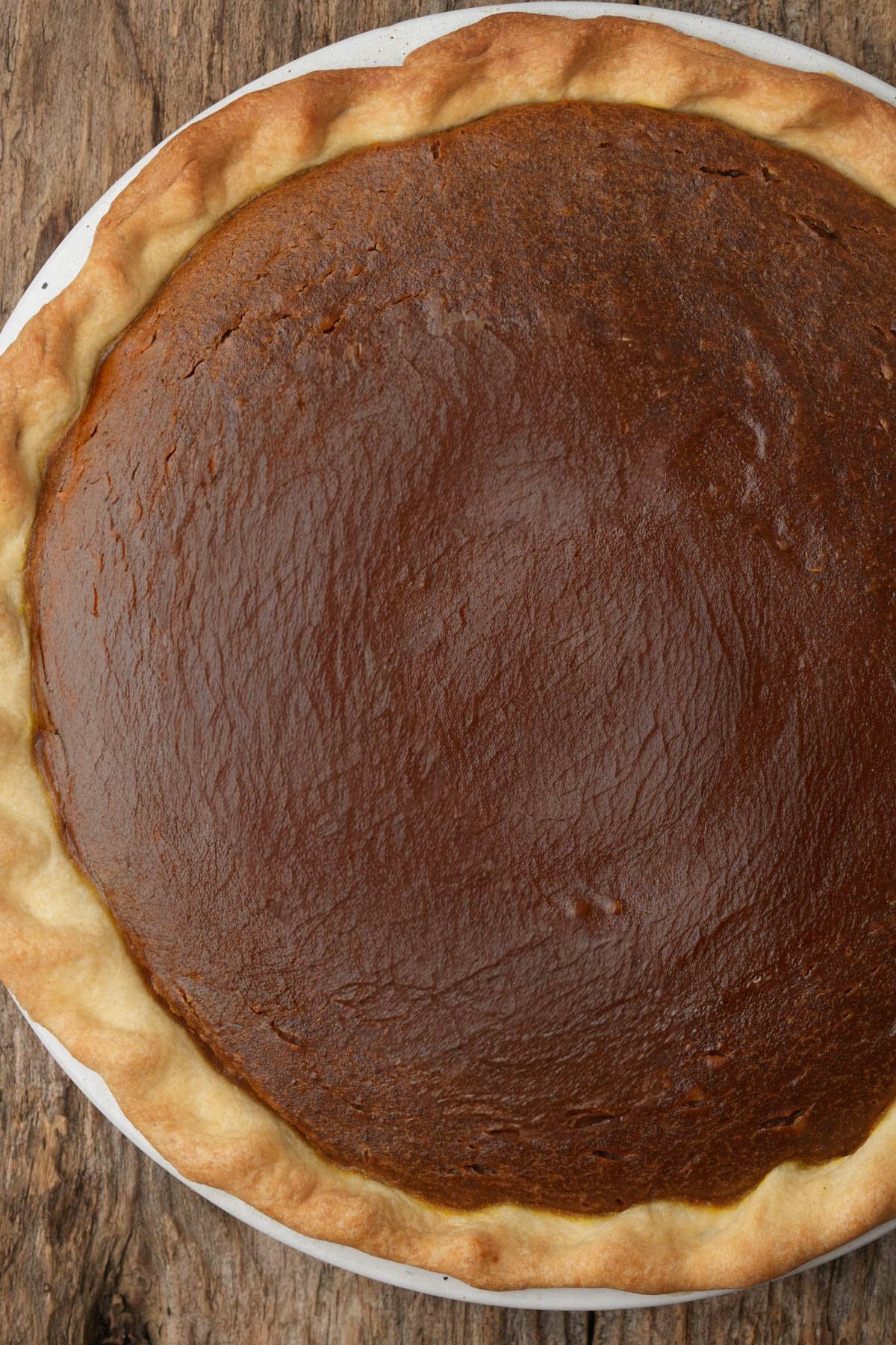 A close-up view of a baked vegan pumpkin pie with a golden-brown crust on a rustic wooden surface.