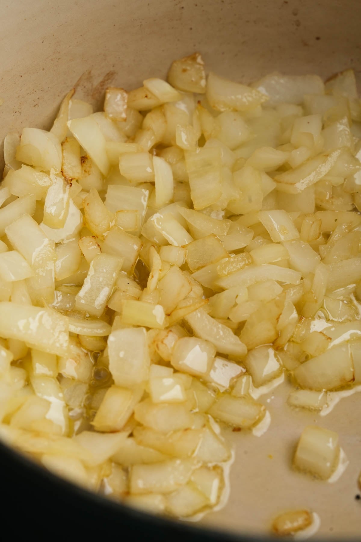 Chopped onions sautéing in oil in a pan, starting to turn translucent with slight browning at the edges.