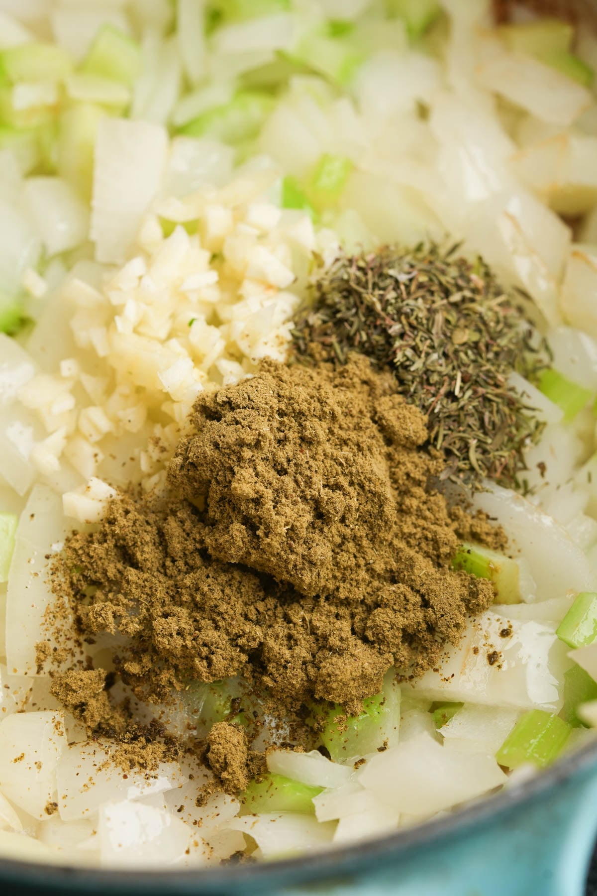 Chopped onions, minced garlic, dried herbs, and a heap of ground spices sit together in a pan, ready to be mixed and cooked.