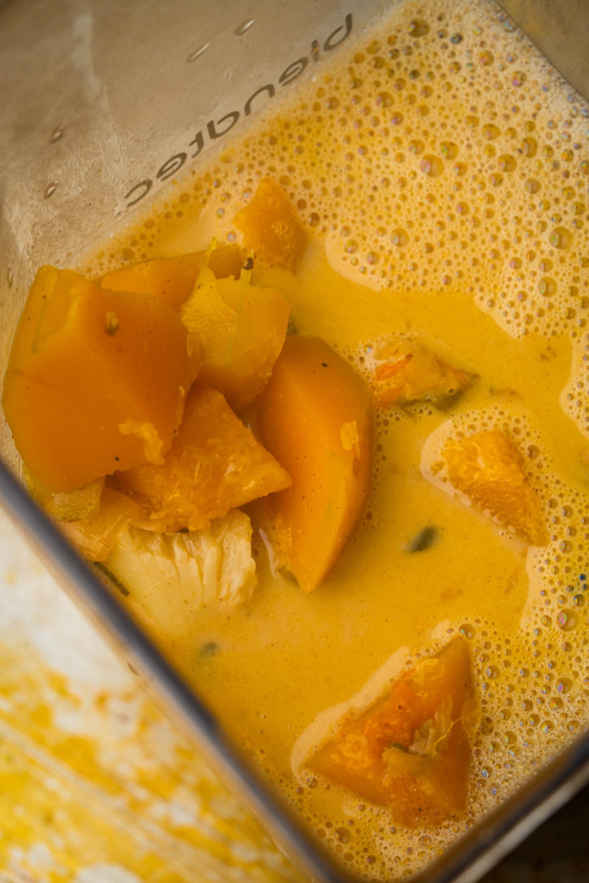 Chunks of orange squash in a creamy, broth inside a blender, ready to be blended into vegan butternut squash soup.