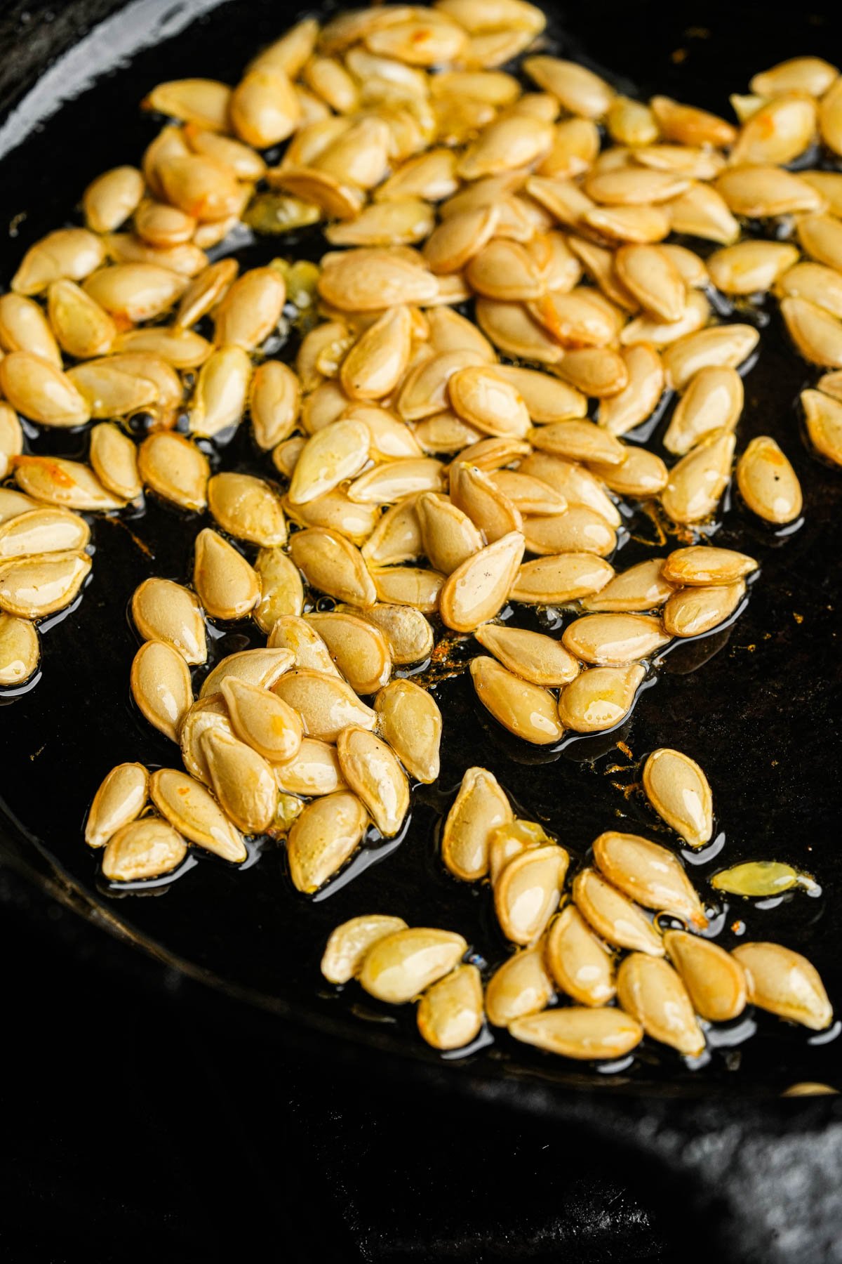 Butternut squash seeds cooking in oil in a black pan.