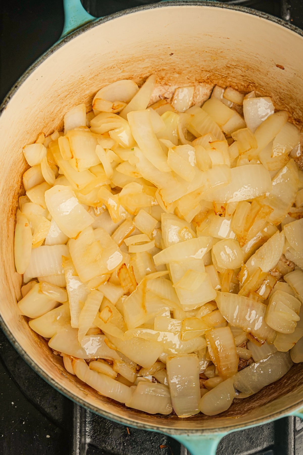 Chopped onions cooking and starting to brown in a large, light-colored pot on a stovetop.